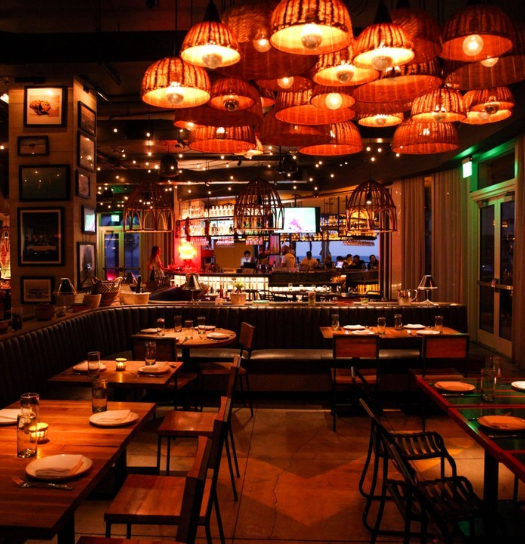 Warm, dimly lit restaurant with hanging lanterns, wooden tables, and bar area.