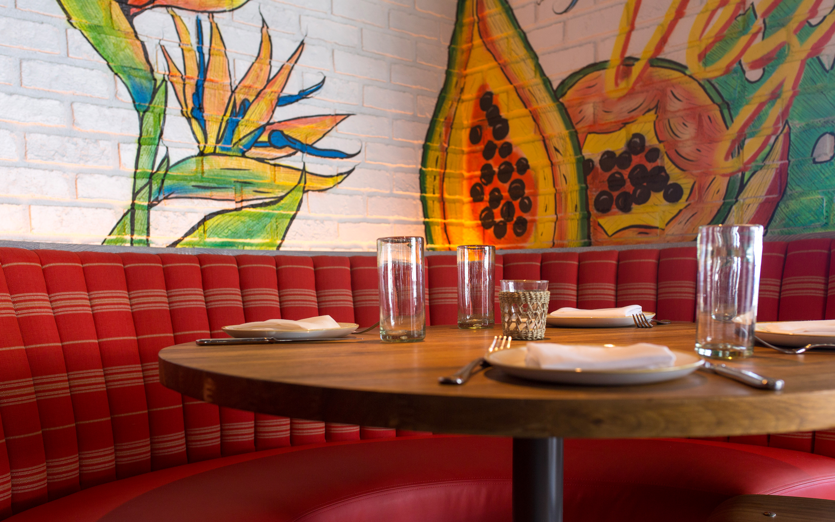 Table with red booth seats and colorful wall painting